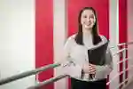 Smiling student holding a folder stands by a railing against red and white background