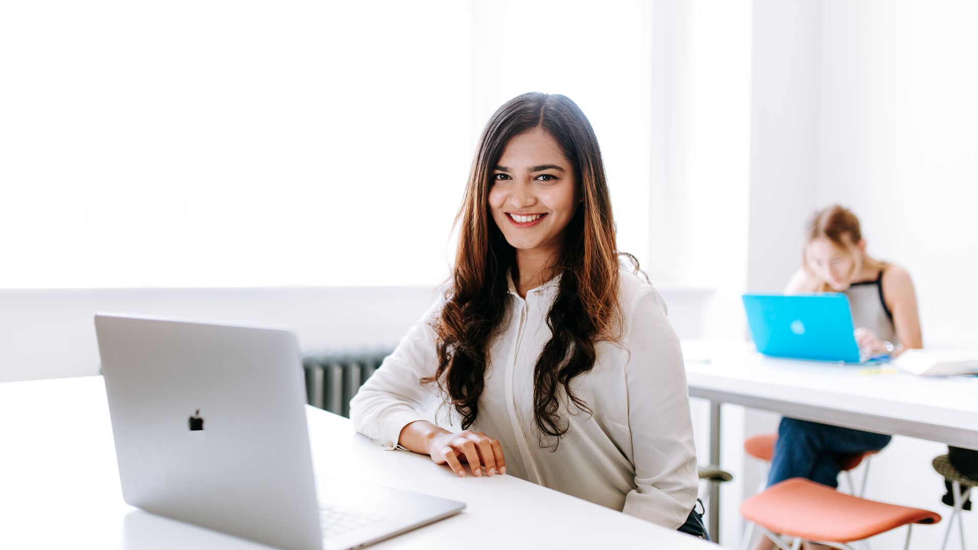Student in a white room smiles at camera with laptop.