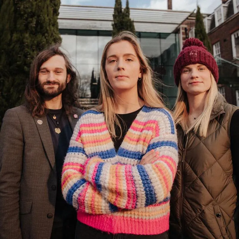 Three of Hull’s academics stand confidently together in front of ferns by the Business School's entrance