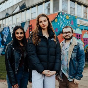 Three of Hull’s students stand confidently together in front of a bright mural on the concrete Wilberforce building