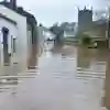 A flooded street with houses either side and a church in the background.