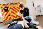 Kneeling student paramedic uses a breathing mask on a mannequin