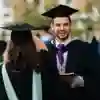 Three students stand chatting in their gowns ahead of a graduation ceremony