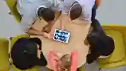 Aerial view looking down on five students gathered around a table looking at scans on a tablet device