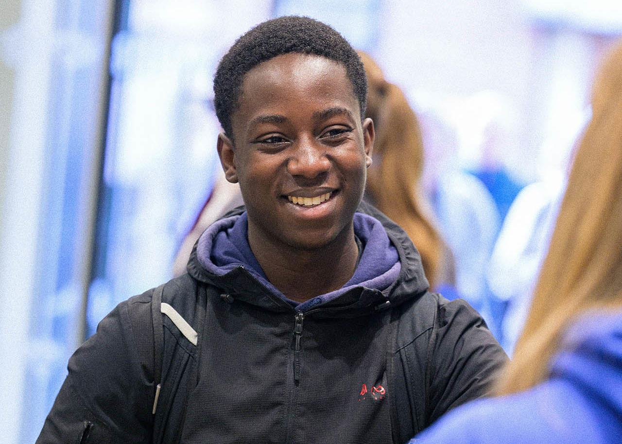 A student wearing a purple hoody and black coat talks to a member of staff at an accommodation event stand