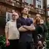 Three students stand confidently in the front courtyard of Wilberforce House against ivy-draped red-brick buildings