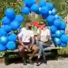 Two students talk and laugh on a bench under a balloon arch outside Westfield Court