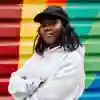 Student flora stands confidently with arms folded in front of a rainbow mural painted on metal shutters