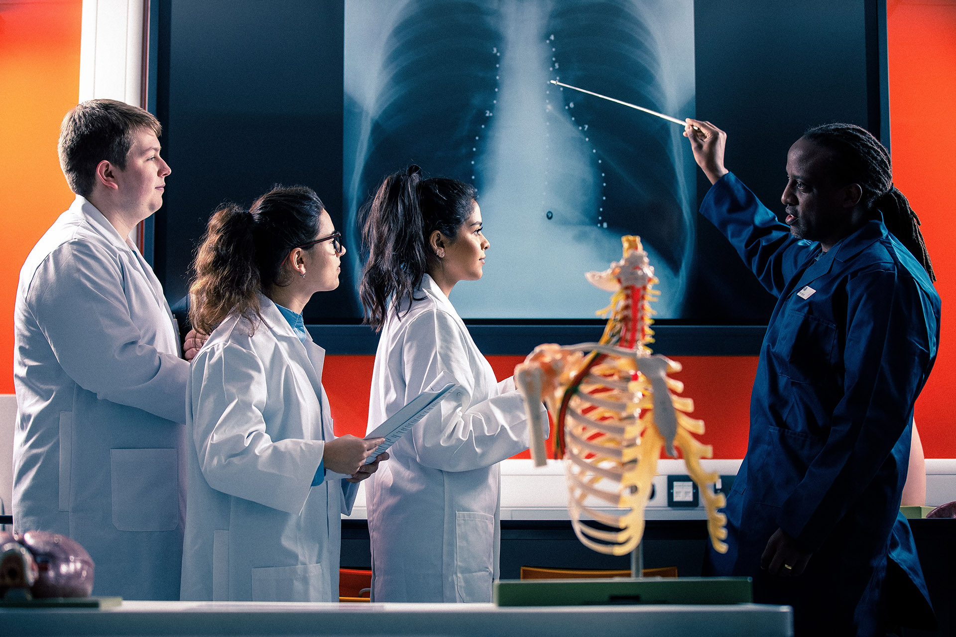An instructor points to an x-ray image while three students in lab coats look on